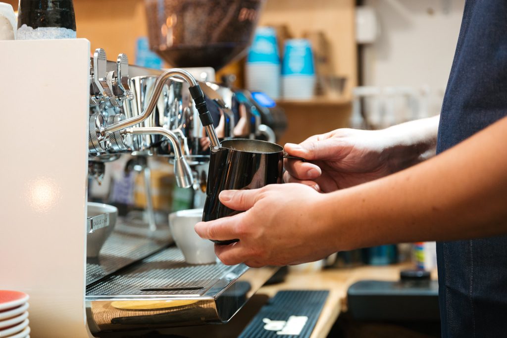 Barista przy ekspresie kolbowym podłączonym do wody i odpływu w kawiarni