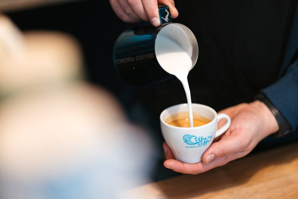 Barista nalewa spienione mleko z dzbanka do filiżanki z espresso
