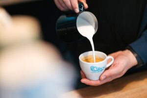 Barista nalewa spienione mleko z dzbanka do filiżanki z espresso