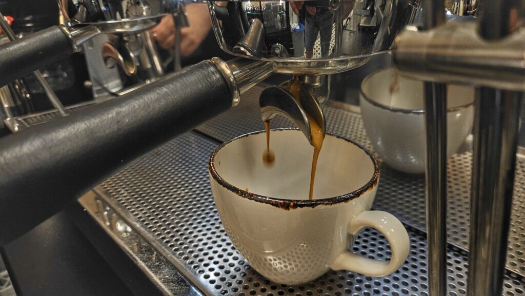 Espresso wypływające cienkim strumieniem z kolby do filiżanki